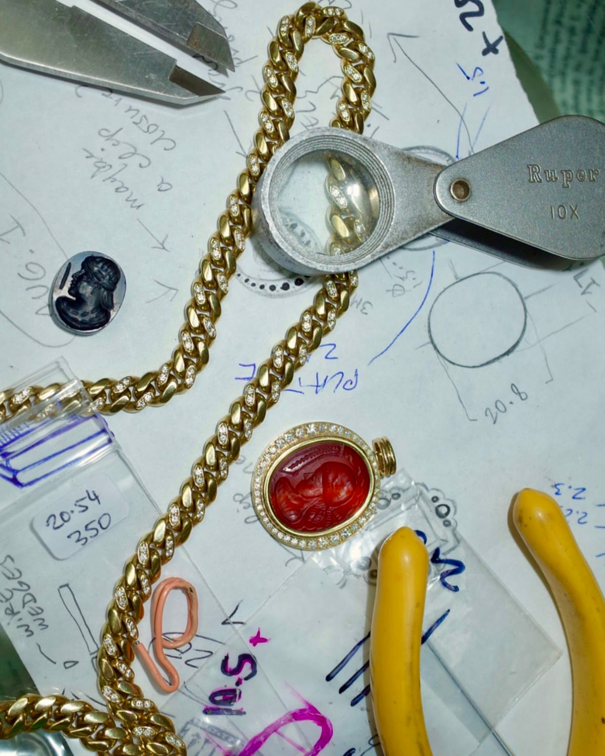 A loupe, measuring gauge, and jewelry pieces atop design sketches and notes