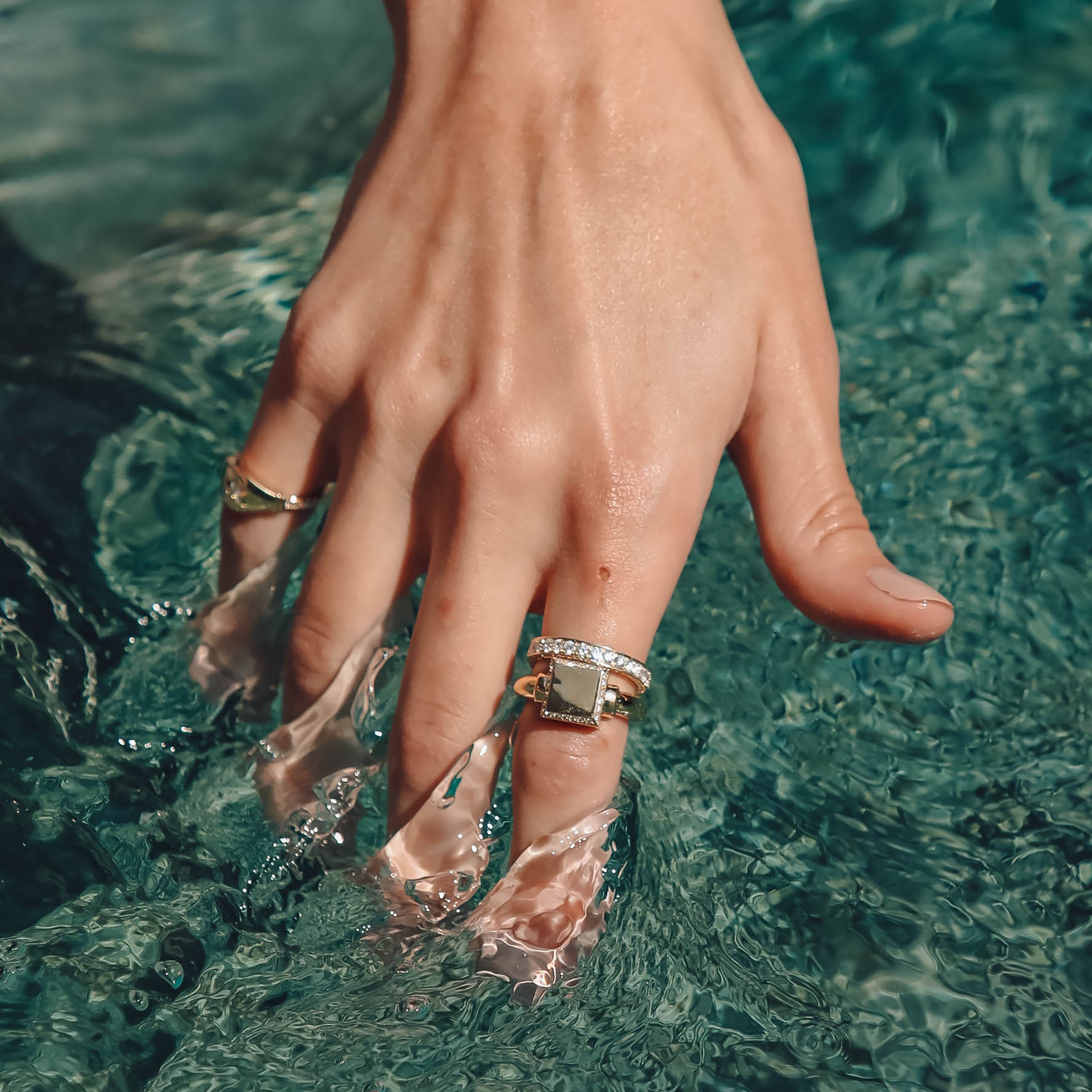 Hand dipping into a pool while wearing the Votum Ring, Large, Scalaria Band, and Maia Star Ring